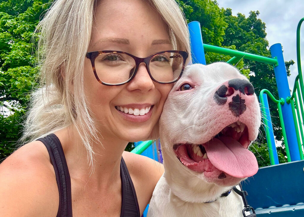 Rachel, a dog walker, is posing at a park with one of the dogs she walks.